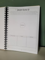 Spiral-bound planner open resting against a green wall