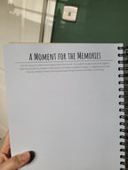 Spiral-bound notebook with text held by a hand on the bottom left-hand corner in front of a blurred background