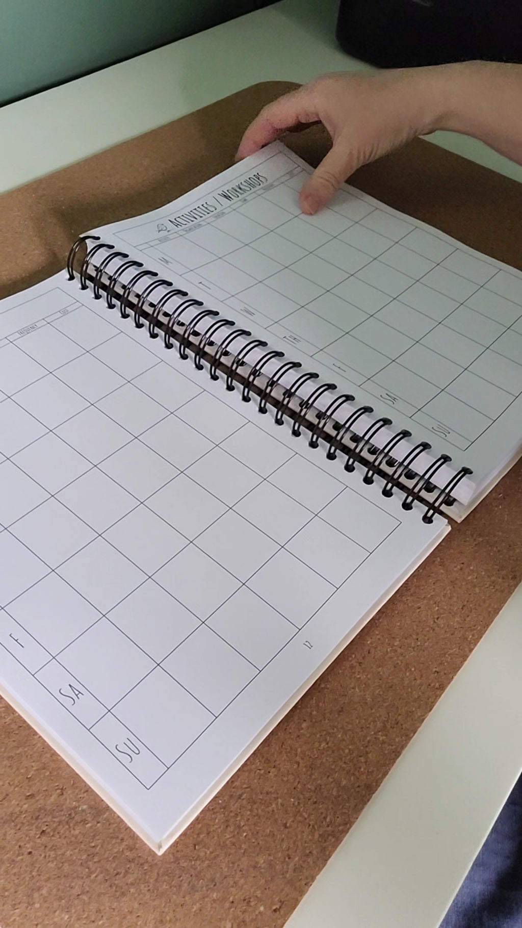 Grid notebook on a cork board with a hand holding the top corner
