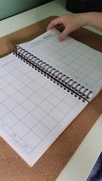Grid notebook on a cork board with a hand holding the top corner